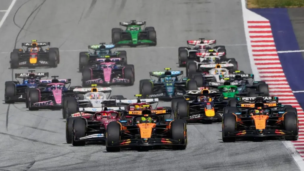 F1 GP Austria 2025 – Lando Norris memimpin rombongan mobil Formula 1 di tikungan pertama Red Bull Ring.